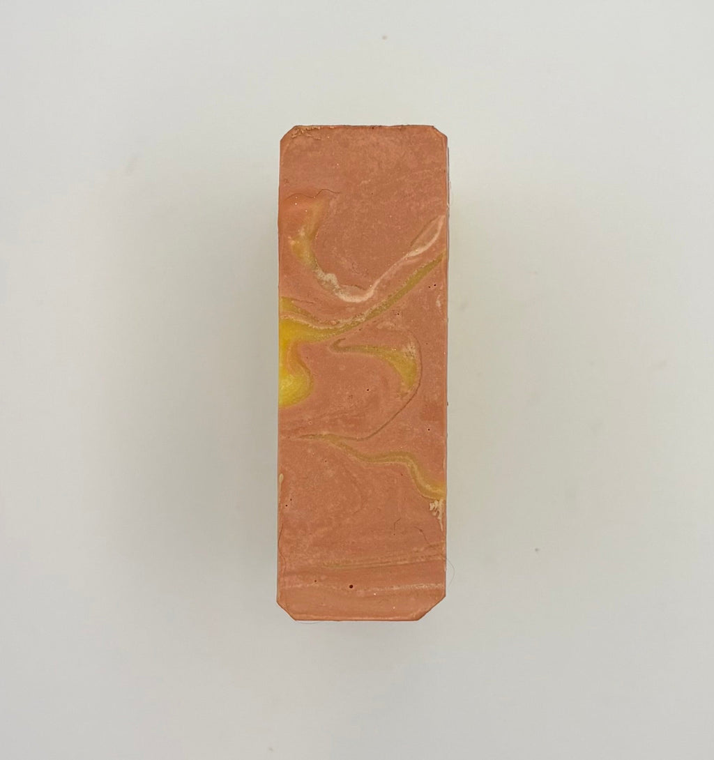 A rectangular bar of soap with a terracotta orange base and marbled yellow and white swirls, centered on a plain light gray background.