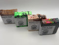 Four artisanal bars of soap from Pleasant Hill Products arranged on a white background. The soaps include Tobacco and Vanilla, Frankinmint, Dracula in Love, and Trick or Treat Cacao and Coffee.